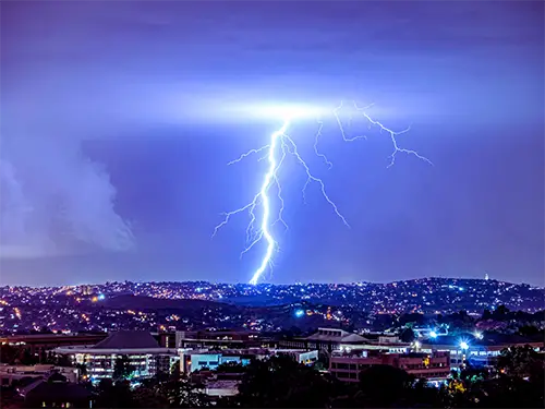 Lightning striking near a residential area, emphasizing the need for surge protection by Tampa Mister Sparky electricians.
